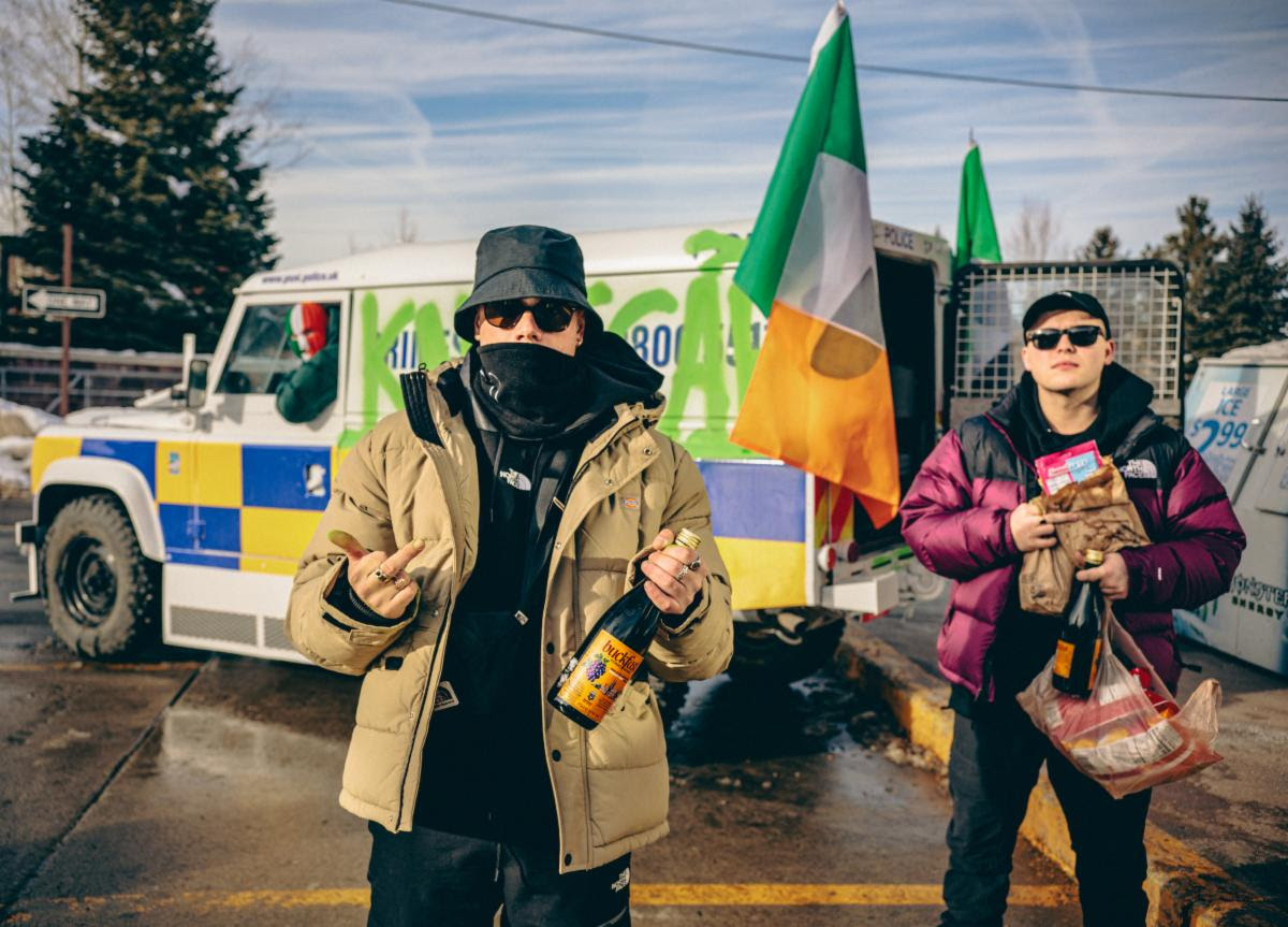 Irish-language hip-hop trio KNEECAP in front of a police car
