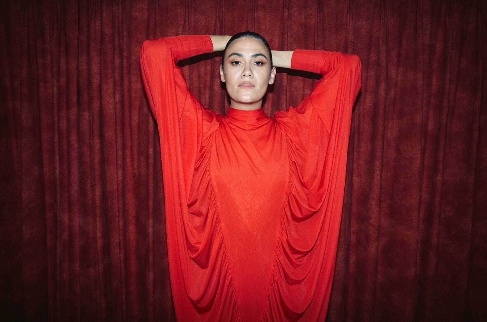 Nadine Shah promotional shot in front of red curtain
