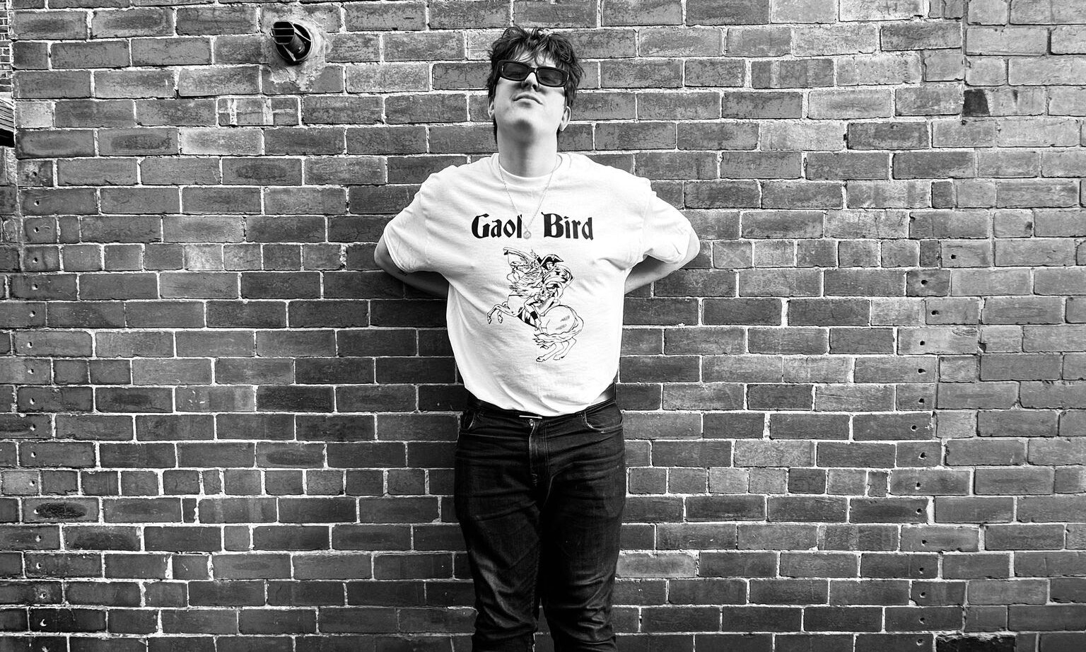 B&W image of Gaol Bird in front of a brick wall